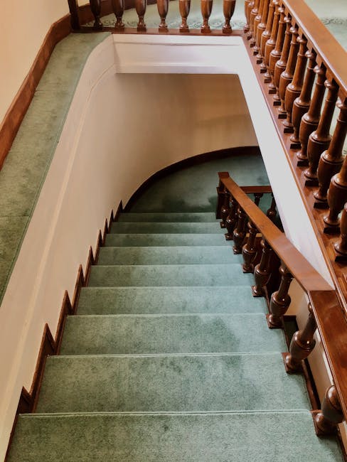 A professional cleaner from Cleaner Finsbury Park is on a stepladder, using a roller attached to an extension pole to clean or re-varnish a large, dark-colored tiled wall in a modern living room. The 