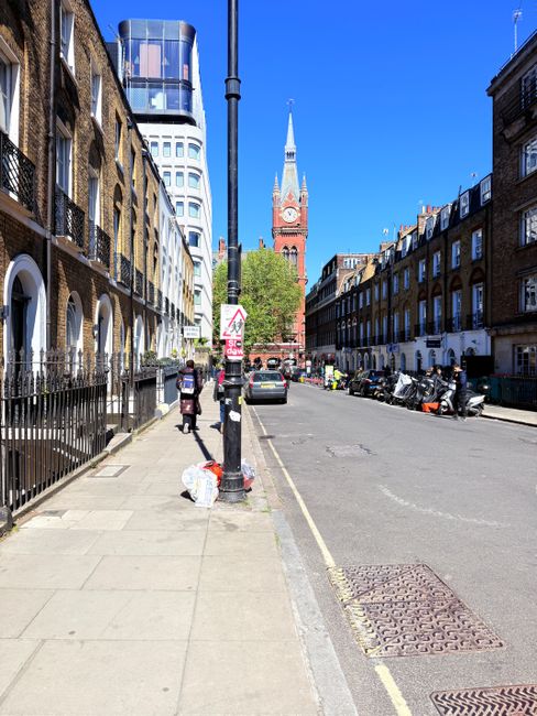 The image depicts a city street scene in Crouch Hill, Finsbury Park, with a clear blue sky overhead. On the left, residential buildings with brick facades feature arched windows and black wrought-iron