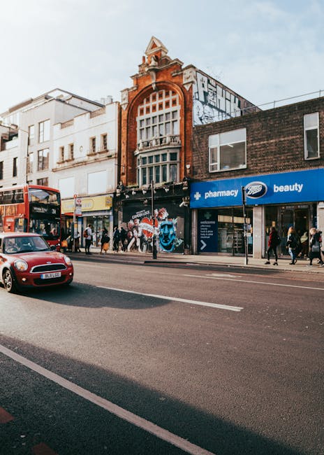The image depicts a city street scene in Crouch Hill, Finsbury Park, with a clear blue sky overhead. On the left, residential buildings with brick facades feature arched windows and black wrought-iron